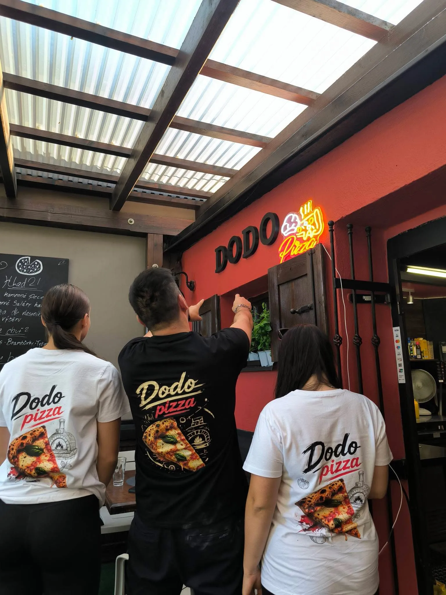 Tým DODO pizza před provozovnou s neonovým nápisem